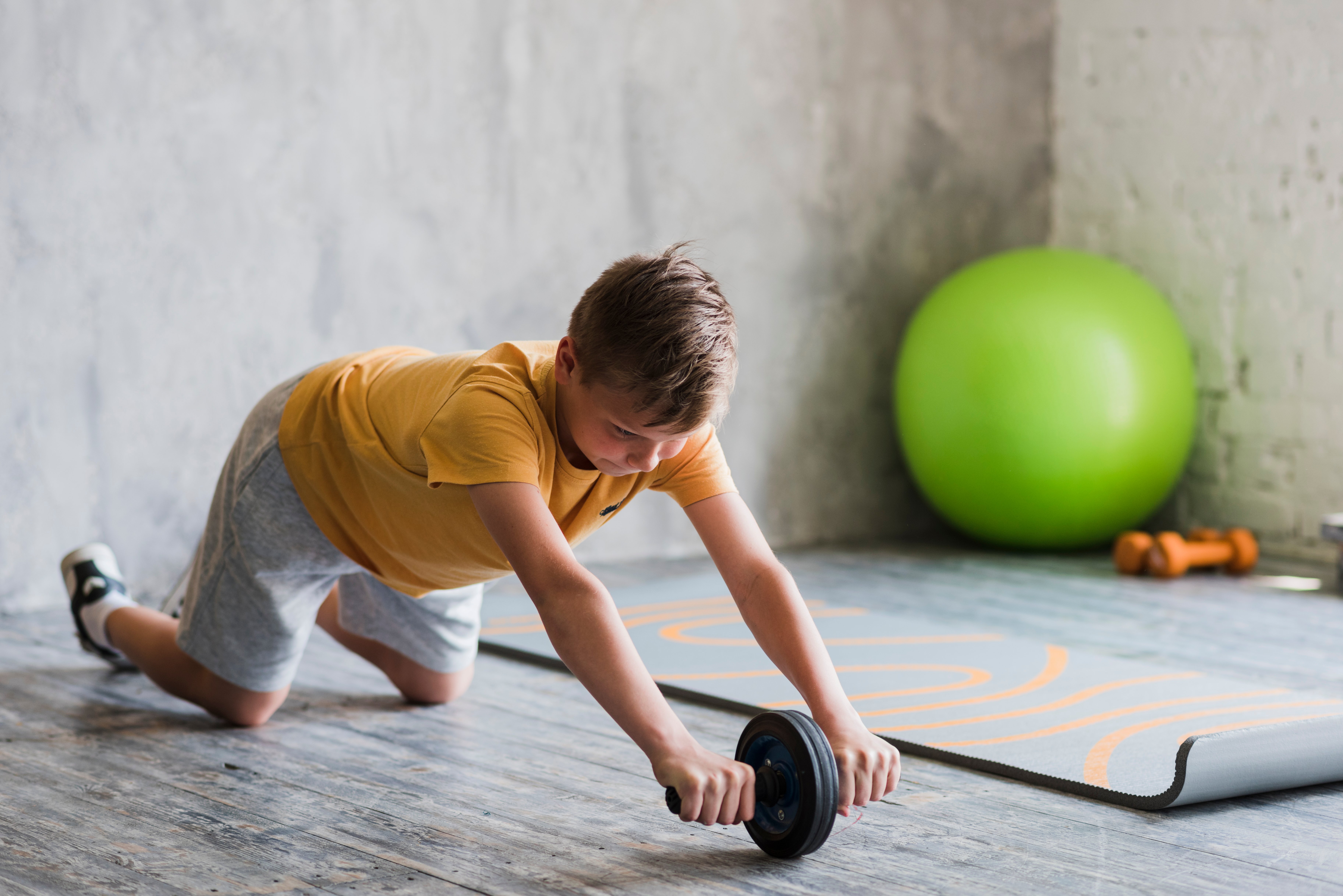 close-up-of-a-boy-doing-ab-wheel-rollout-exercise-on-hardwood-floor