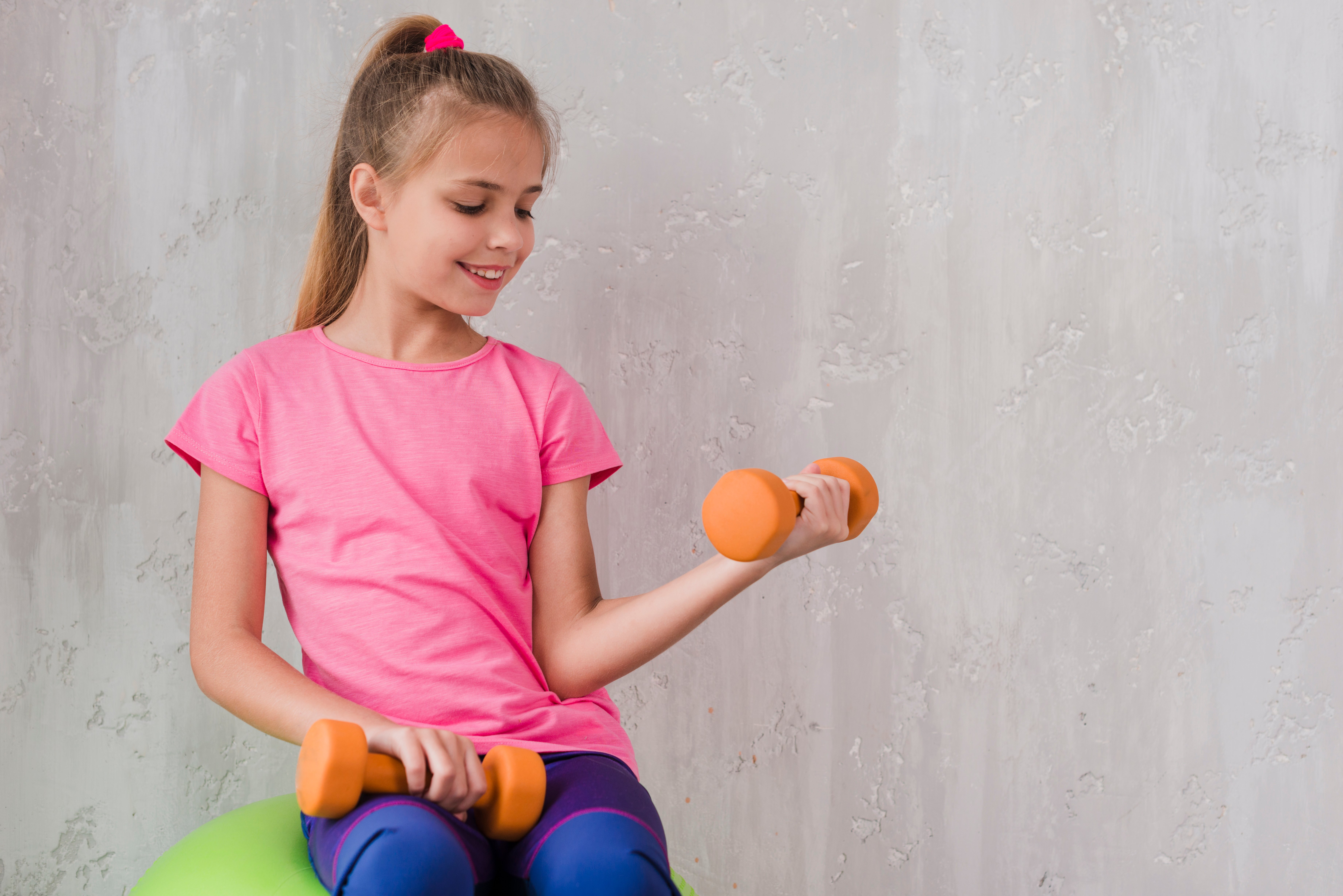 smiling-portrait-of-a-girl-exercising-with-dumbbell-against-wall